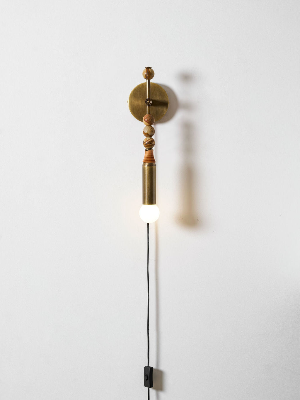 Clérachic wall light on a plain wall, mixed-size wood beads above a lit glass globe and a trailing cord.