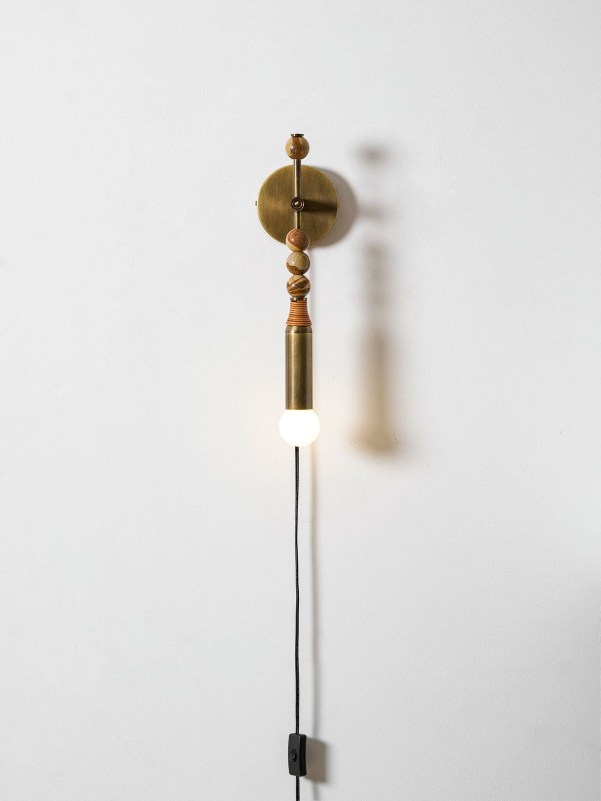 Clérachic wall light on a plain wall, mixed-size wood beads above a lit glass globe and a trailing cord.