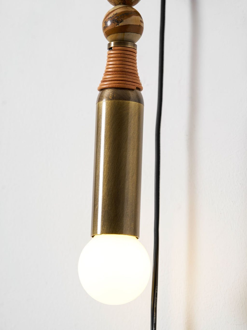 Close-up of a Clérachic wall lamp's brass socket tube and lit glass globe bulb, cord visible against the wall.