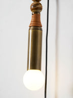 Close-up of a Clérachic wall lamp's brass socket tube and lit glass globe bulb, cord visible against the wall.