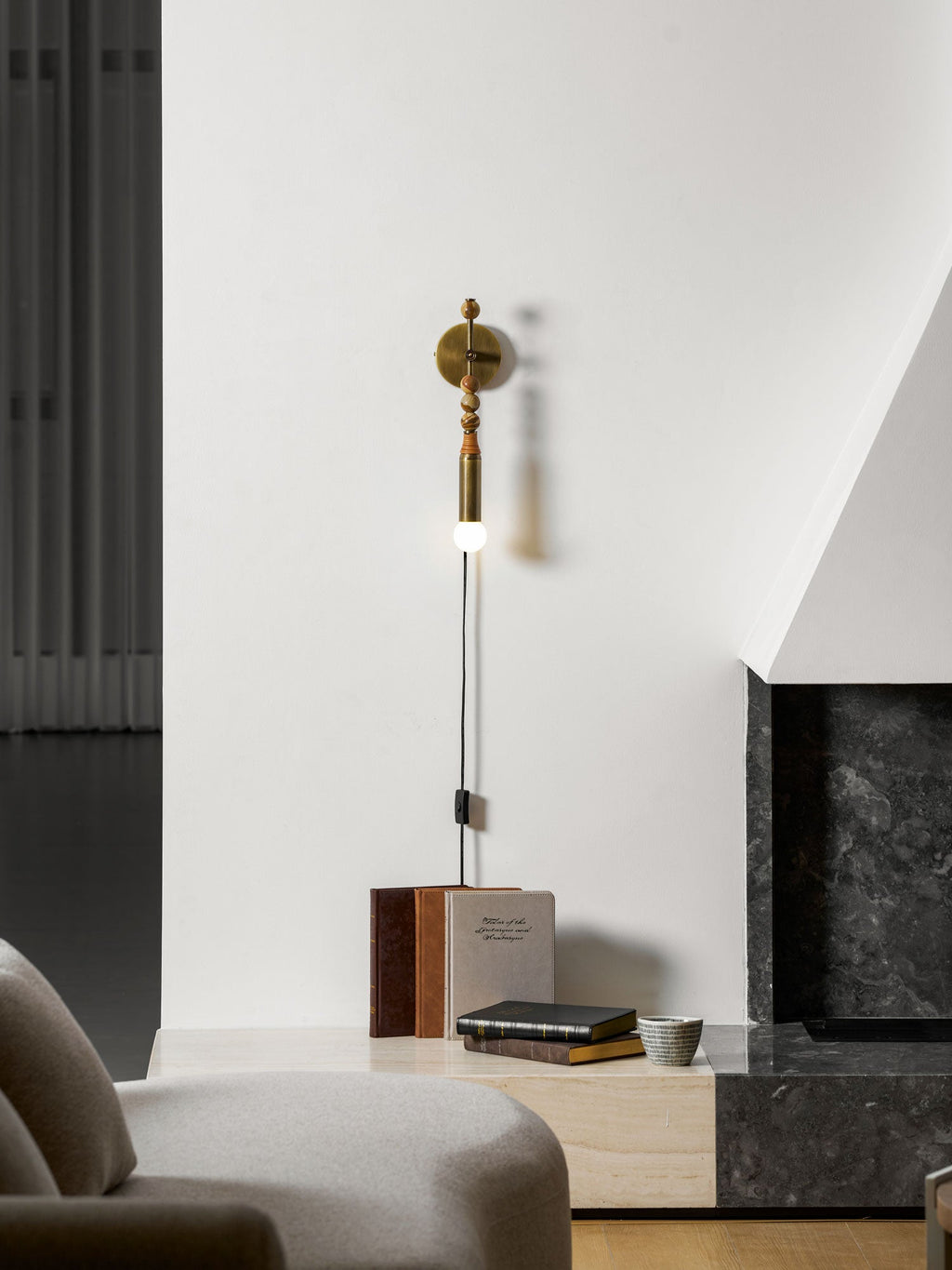 Clérachic wall sconce in a lounge corner beside a sofa and a side table stacked with books, wood beads lit.
