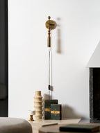 Clérachic plug-in wall lamp in a lounge corner, dark beads above a lit globe, a ceramic vase and books nearby.