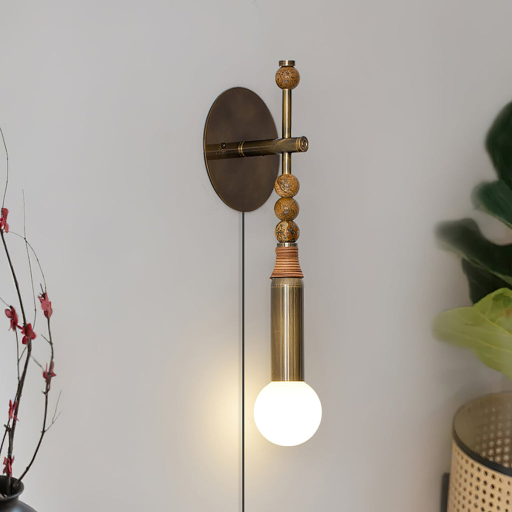 Clérachic wall sconce mounted on a pale wall beside a leafy branch, warm wood beads above its glowing glass globe.
