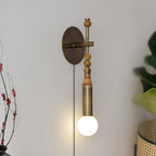 Clérachic wall sconce mounted on a pale wall beside a leafy branch, warm wood beads above its glowing glass globe.