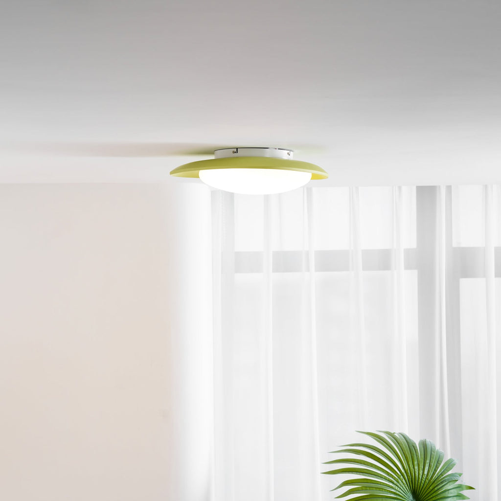 Close to a sheer curtain and a potted palm, the white diffuser of this Clérachic ceiling light is visible from below.