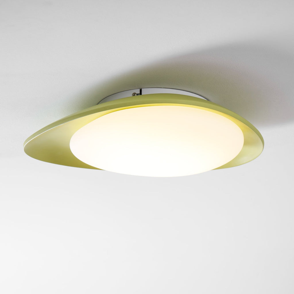 On a plain grey backdrop, this Clérachic ceiling light's green resin body wraps around a lit white diffuser.