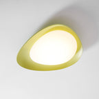 From a raised angle on a grey backdrop, this Clérachic ceiling light shows its asymmetric green resin rim glowing warm.