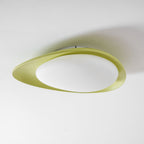 Seen from an angle, the green resin body of this Clérachic ceiling light frames a glowing oval diffuser.