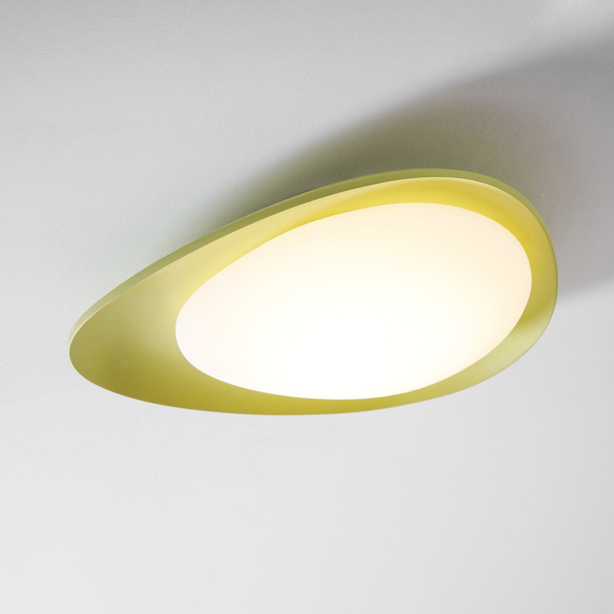 From a low angle on a plain backdrop, this Clérachic ceiling light's green rim glows warm around its diffuser.