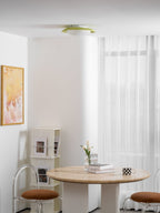 In a bright room with a framed print and a round table set with books and a vase, this Clérachic ceiling light sits in the ceiling corner.