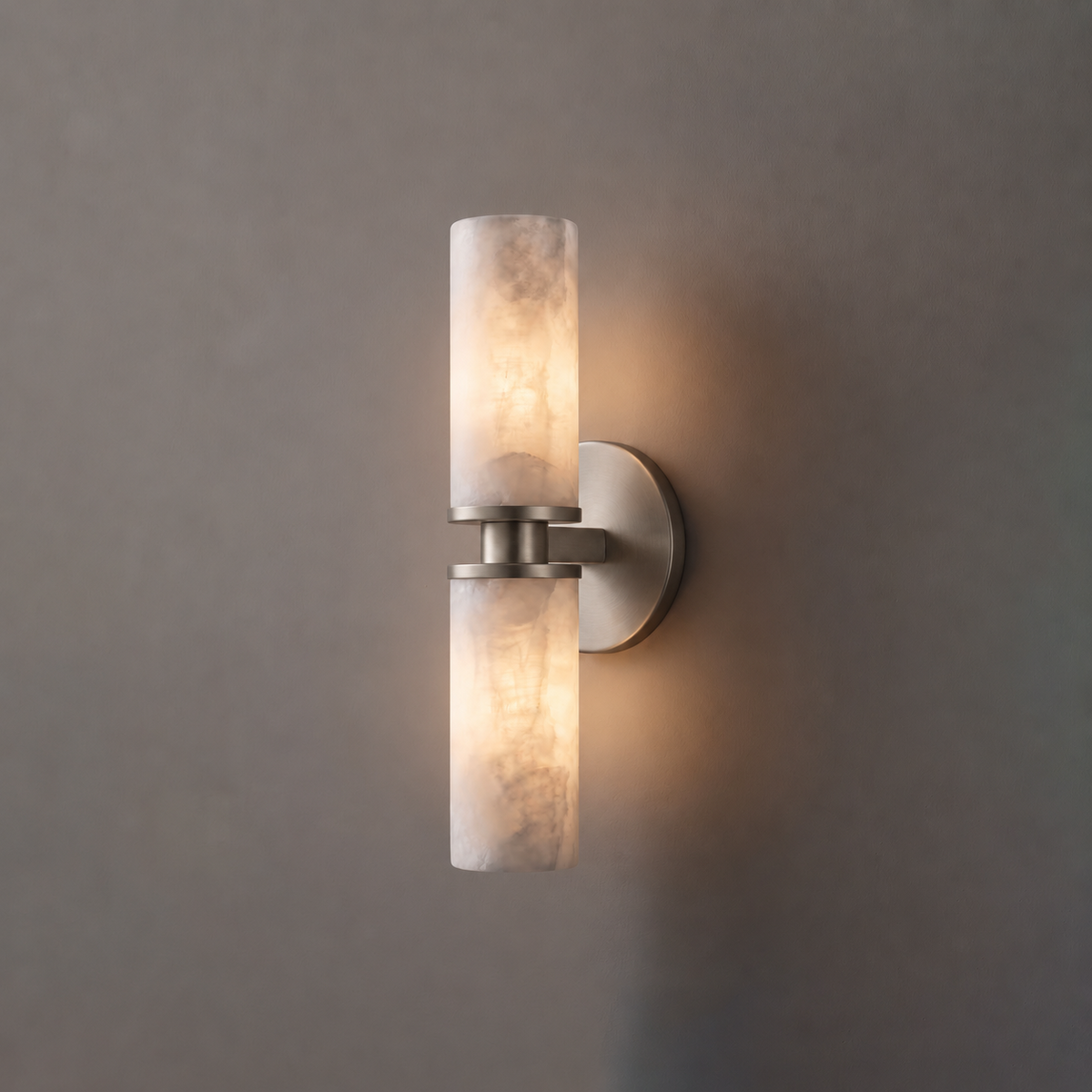 Close product view of this Clérachic wall light in brushed nickel, its two alabaster tubes lit against grey.