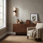 In a room with a walnut credenza styled with pottery, this Clérachic wall light in matte black glows on a plaster wall.