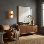 Beside a large abstract print above a walnut credenza, this Clérachic wall light in brushed brass glows softly.