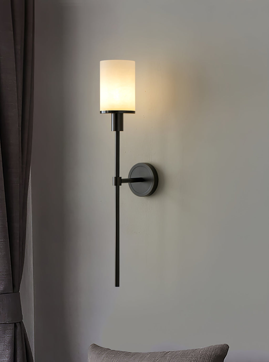 Clérachic dark bronze alabaster sconce lit beside a grey curtain, a soft cushion just below the frame
