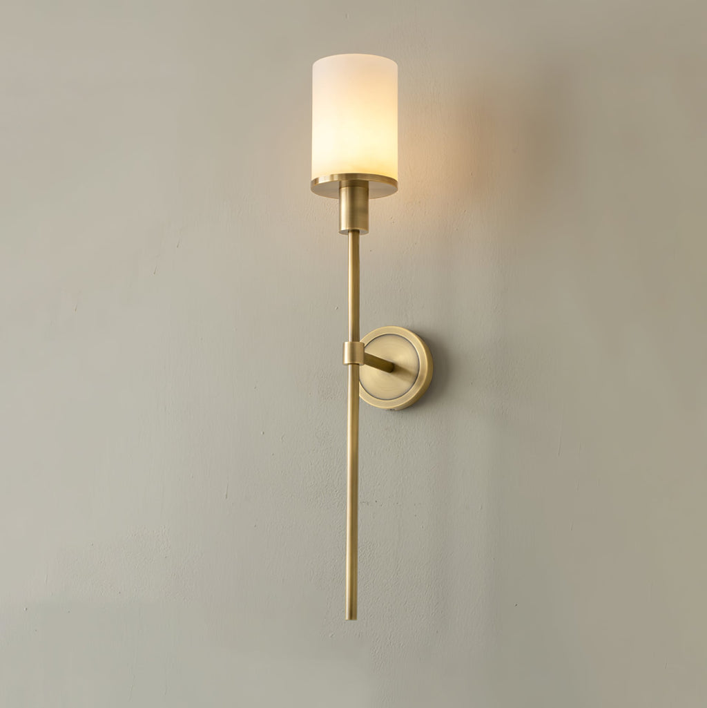 Clérachic brass alabaster sconce seen three-quarter on a sage plaster wall, opal shade warmly lit