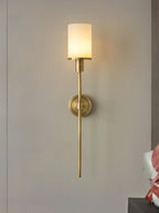 Clérachic brass alabaster sconce lit on a grey wall, shown at a slight angle from the right