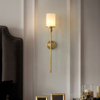 Clérachic brass alabaster sconce lit beside a studded headboard on a panelled bedroom wall
