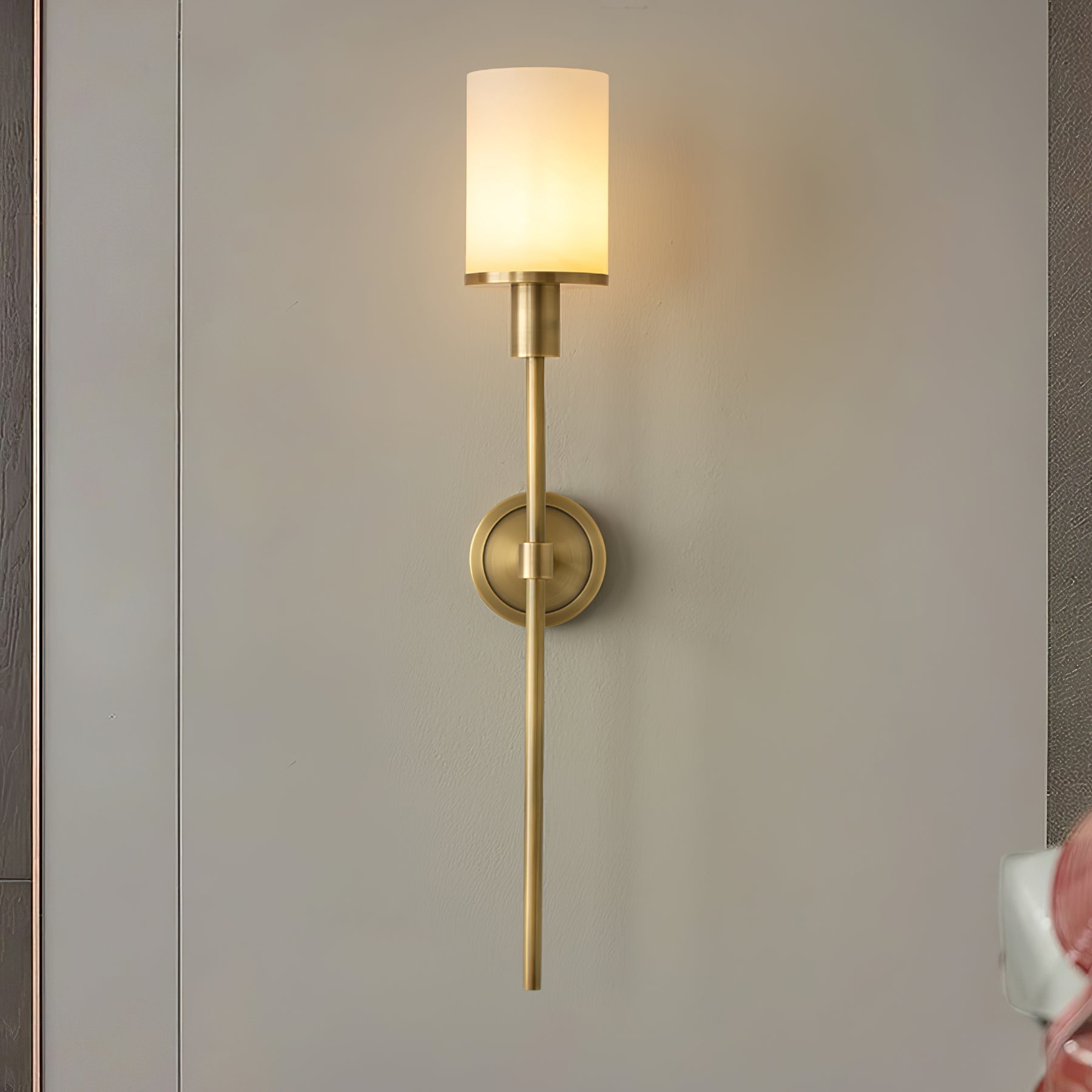 Clérachic brass alabaster sconce lit on a grey wall panel between dark timber uprights