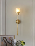 Clérachic brass alabaster sconce lit on a panelled wall above framed art, a plaster bust and hydrangeas