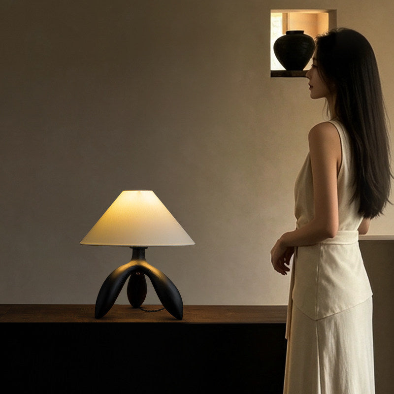 On a low cabinet beneath a floating shelf, this dark wood Clérachic lamp glows as a figure moves past in white.