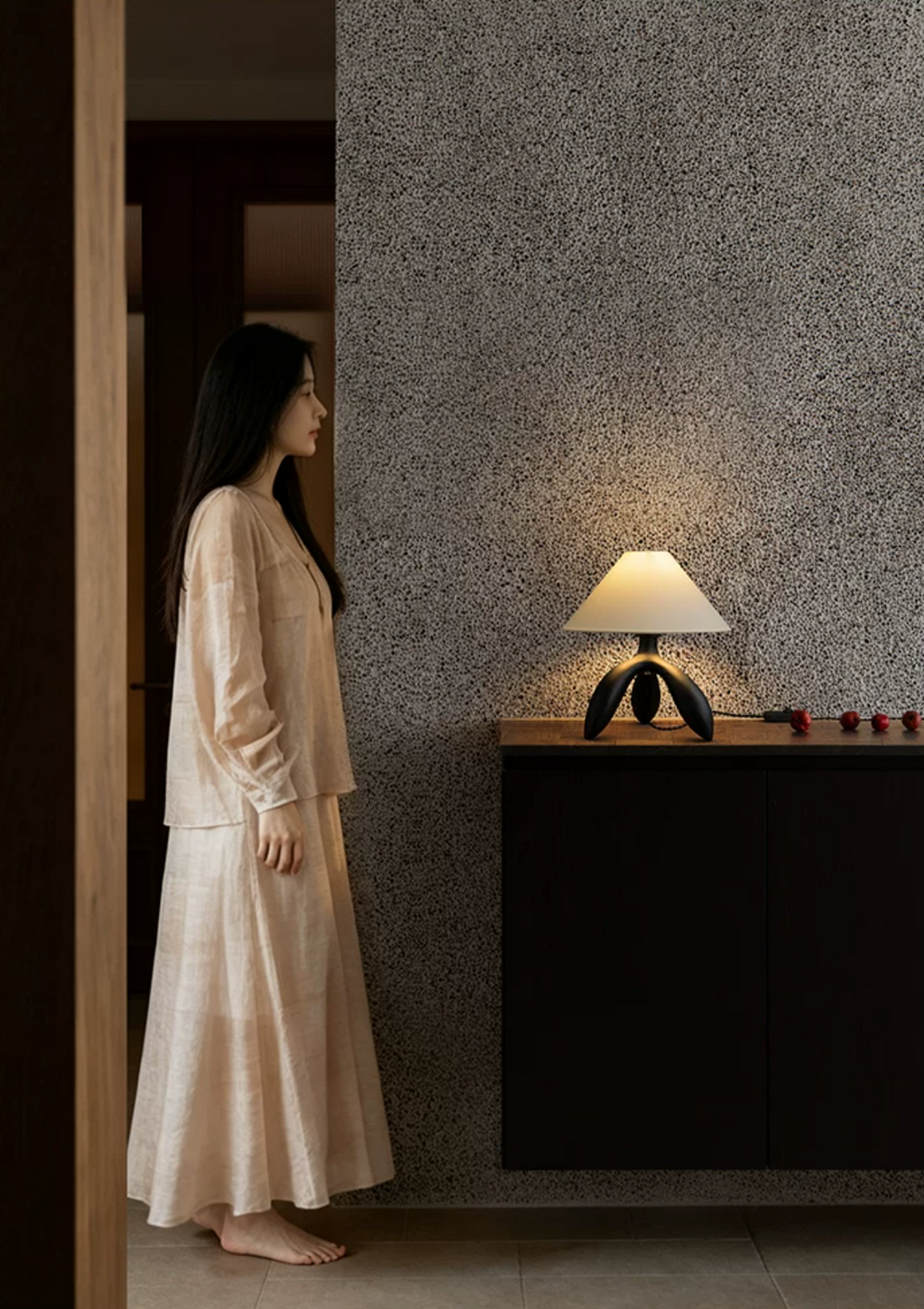 In a textured hallway, this dark wood Clérachic lamp glows on a low cabinet near a doorway.