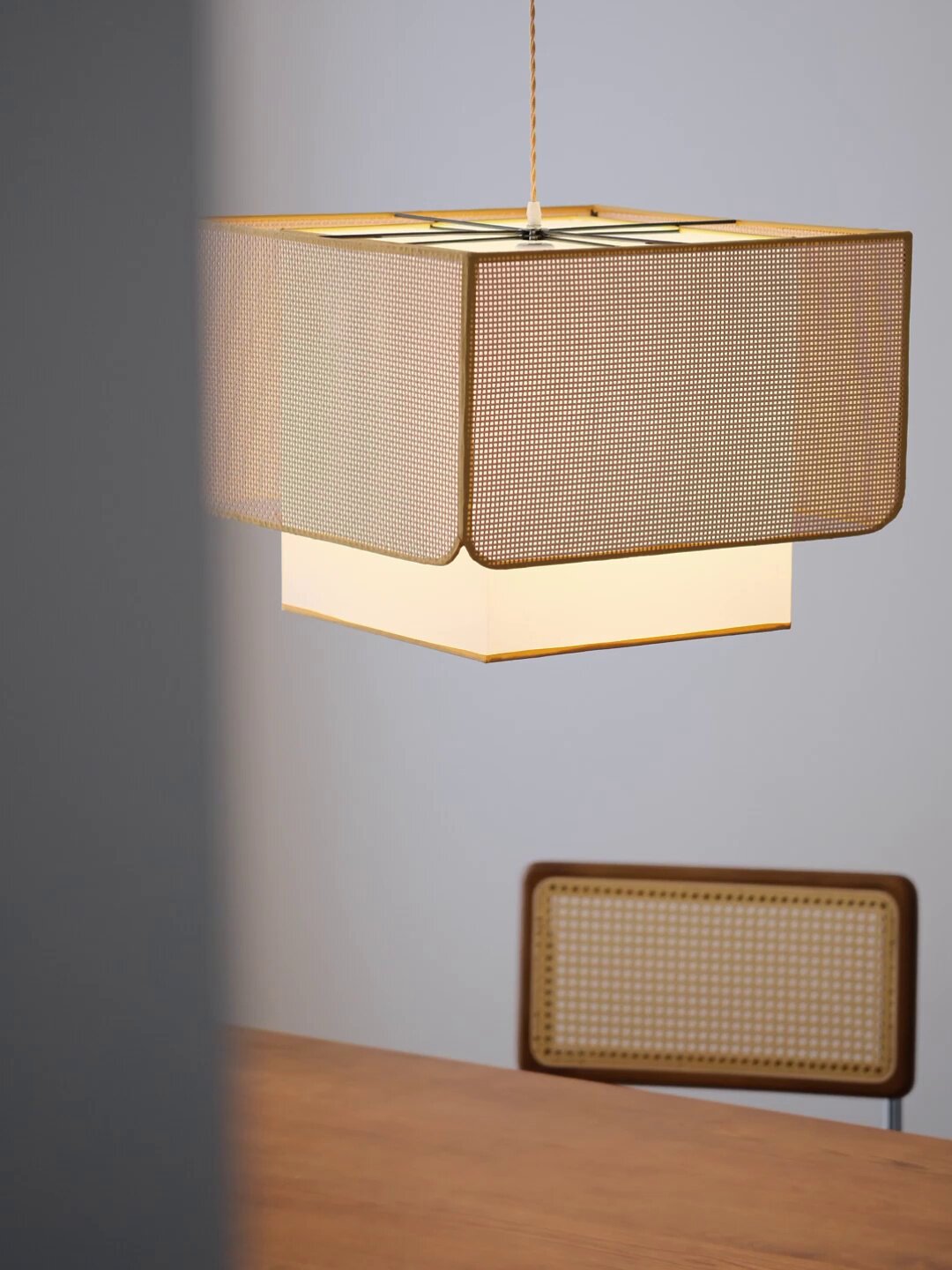 Close angle on this Clérachic pendant's rattan lattice weave, glowing above a wood bench with a woven panel.