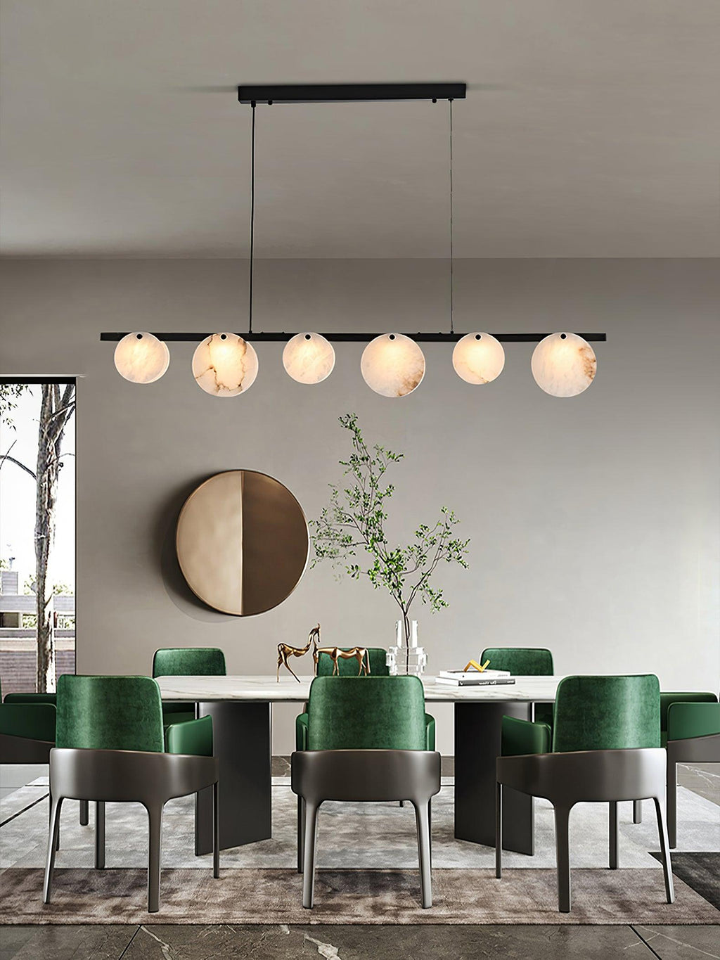 Lit above a dining table with green velvet chairs, a round brass mirror on the wall behind.