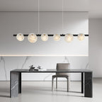 The chandelier lit above a black marble dining table in a white marble-lined room.