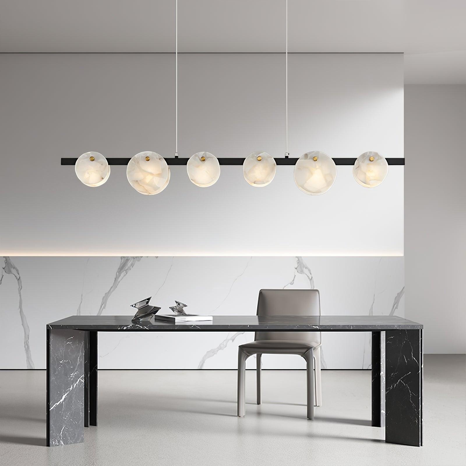 The chandelier lit above a black marble dining table in a white marble-lined room.