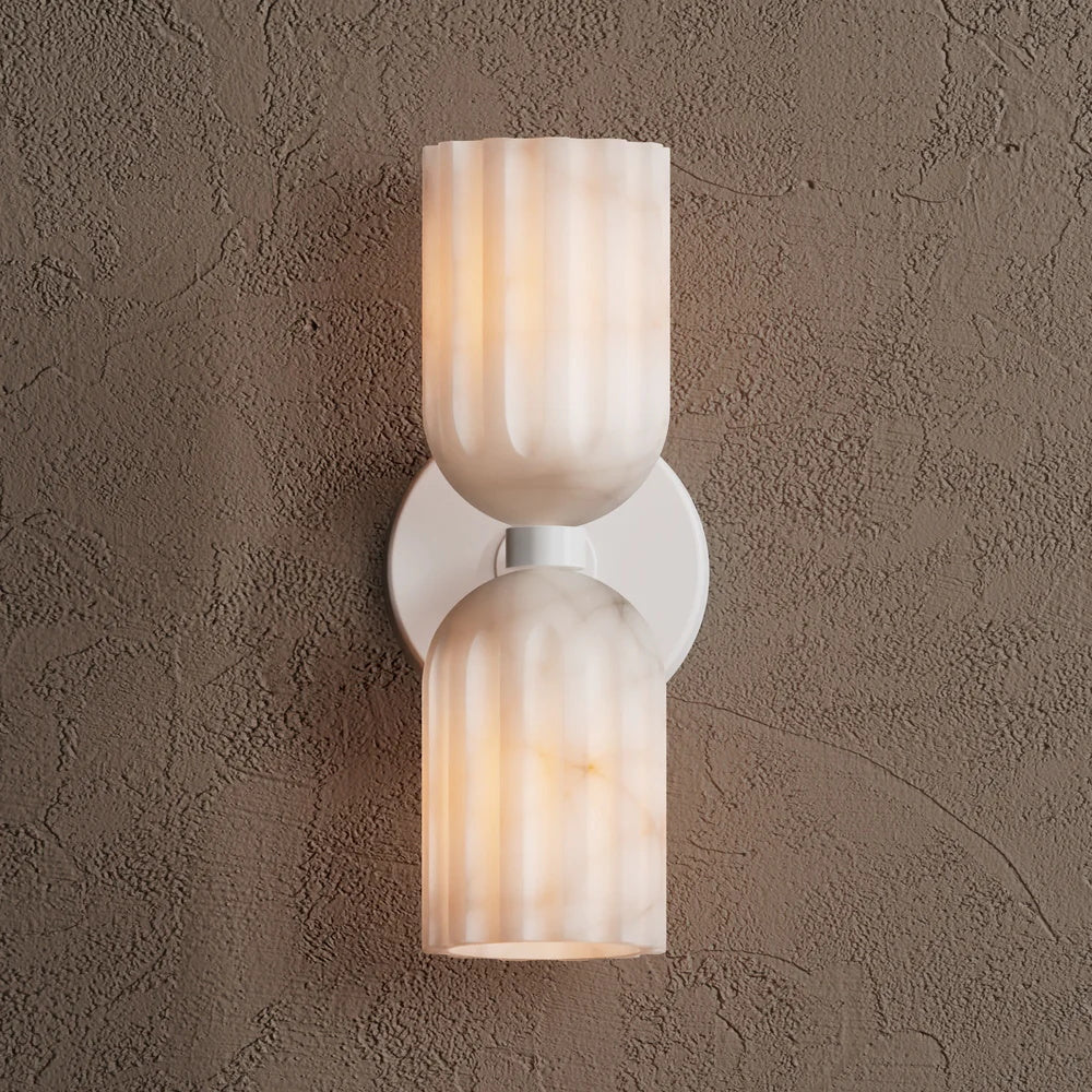 Front view of the white sconce, its two fluted alabaster shades glowing softly