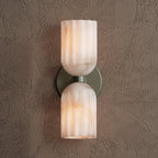 Sage green double sconce with fluted alabaster shades glowing warm amber, straight-on view