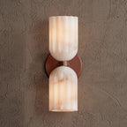 Double alabaster wall sconce in terracotta, lit and photographed straight on against a plaster wall