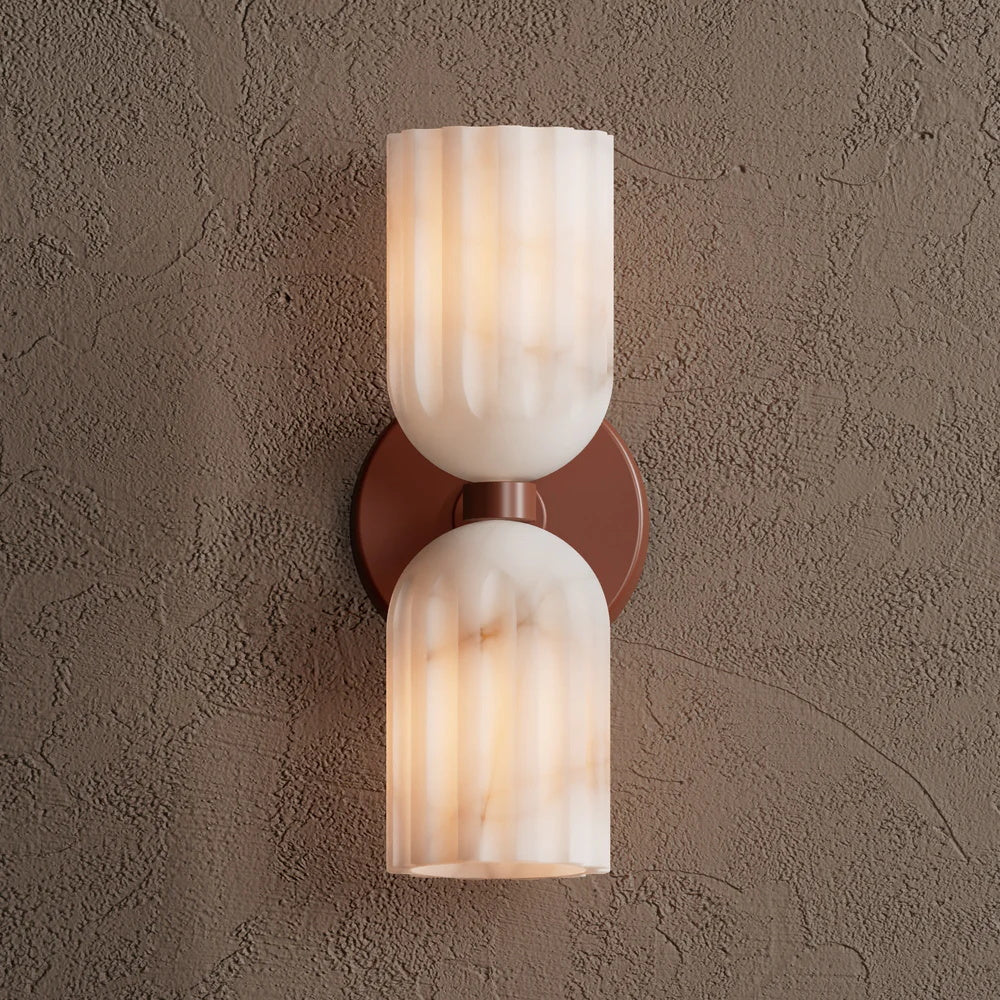 Double alabaster wall sconce in terracotta, lit and photographed straight on against a plaster wall