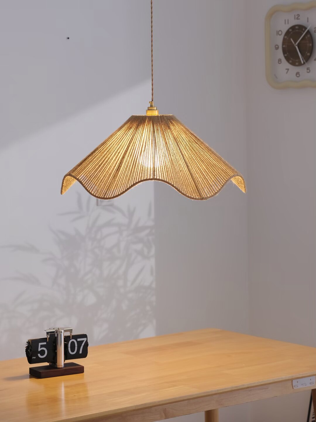 A flip clock and round wall clock sit near this lit Clérachic pendant on a plain wood table.