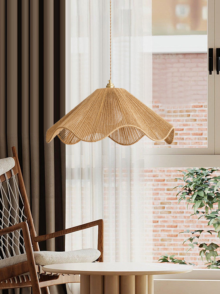 A rattan chair sits near this lit Clérachic pendant, with a brick building visible through sheer curtains behind.