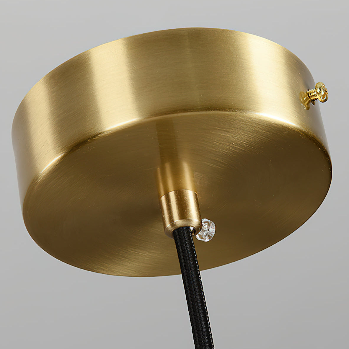 Close-up of the brushed brass ceiling canopy with the black fabric cord running through it.