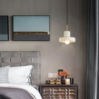 Ritta hat-shaped pendant lit beside a bed, hanging over a nightstand below framed artwork.