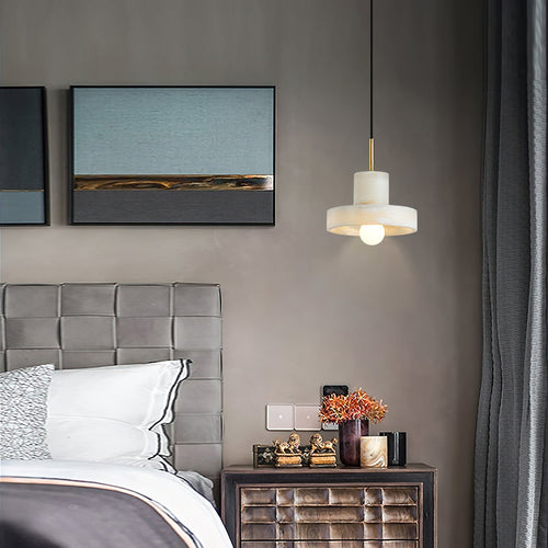 Hat-shaped pendant lit beside a bed, hanging over a nightstand below framed artwork.