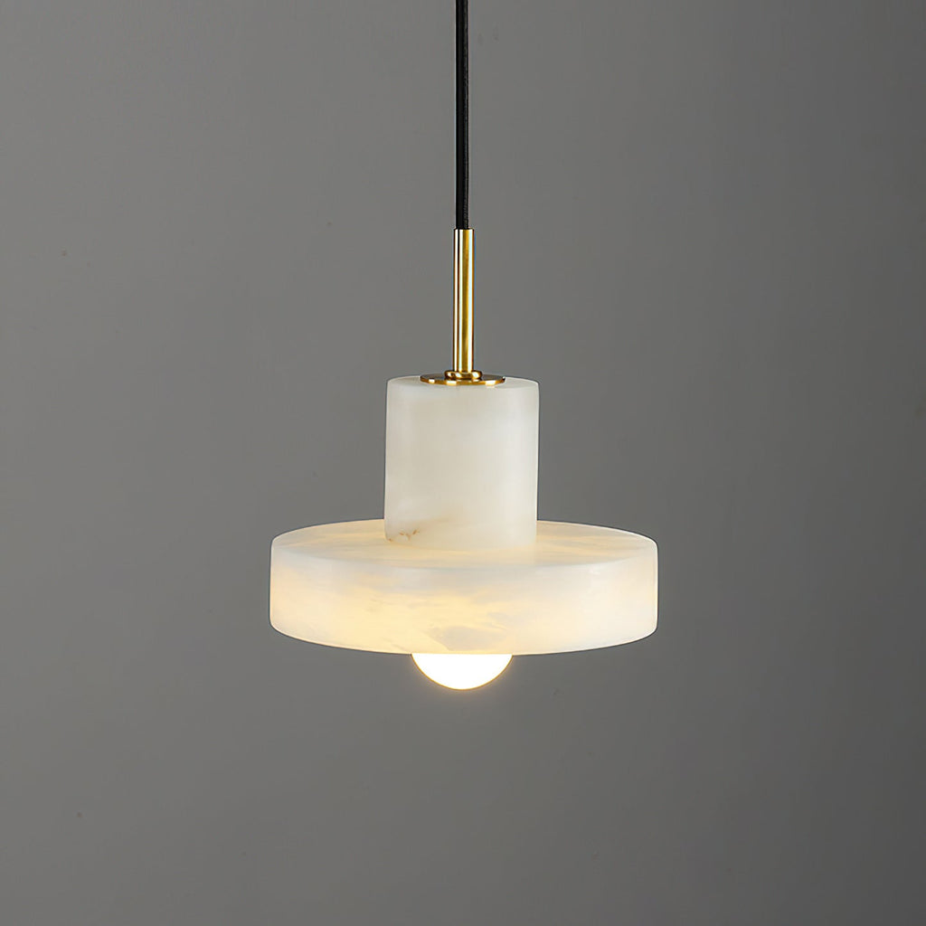 Close studio view of the lit Ritta pendant, brass stem meeting the alabaster cylinder and brim.
