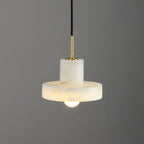 Close studio view of the lit Ritta pendant, brass stem meeting the alabaster cylinder and brim.