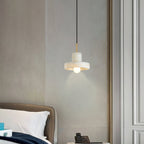 Ritta pendant glowing beside a quilted headboard, its bulb throwing a soft cone onto the wall.