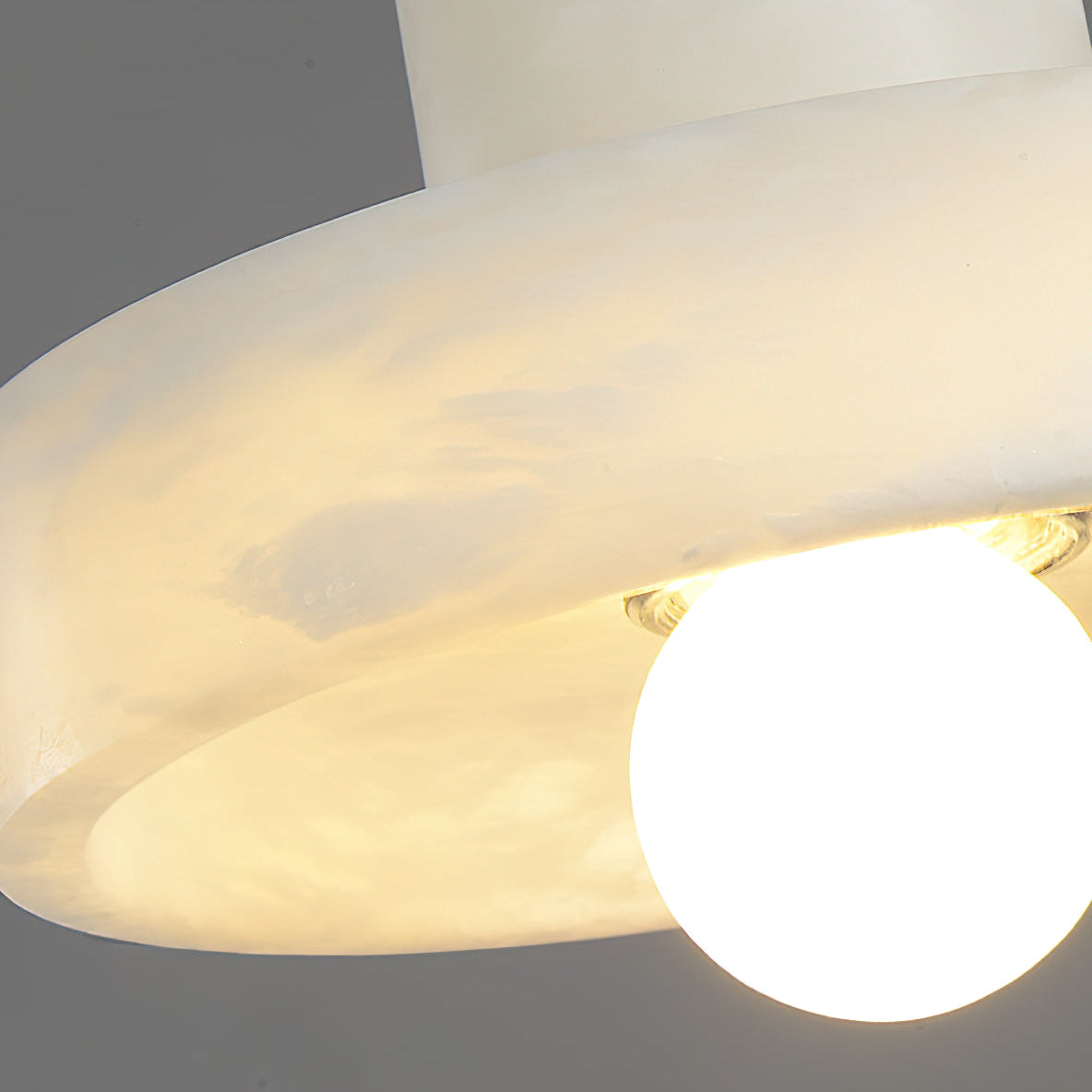 Angled close-up of the alabaster brim edge with warm light spilling past the globe bulb.