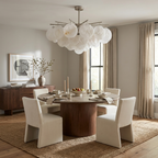 This nickel Clérachic chandelier hangs above a round wood dining table circled by cream upholstered chairs.