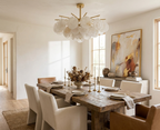 Brass candlesticks and a low floral centerpiece sit beneath this Clérachic chandelier in a rustic dining room.