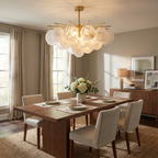 White flowers sit on a dining table beneath this brass Clérachic chandelier, glowing warm in a sunlit room.
