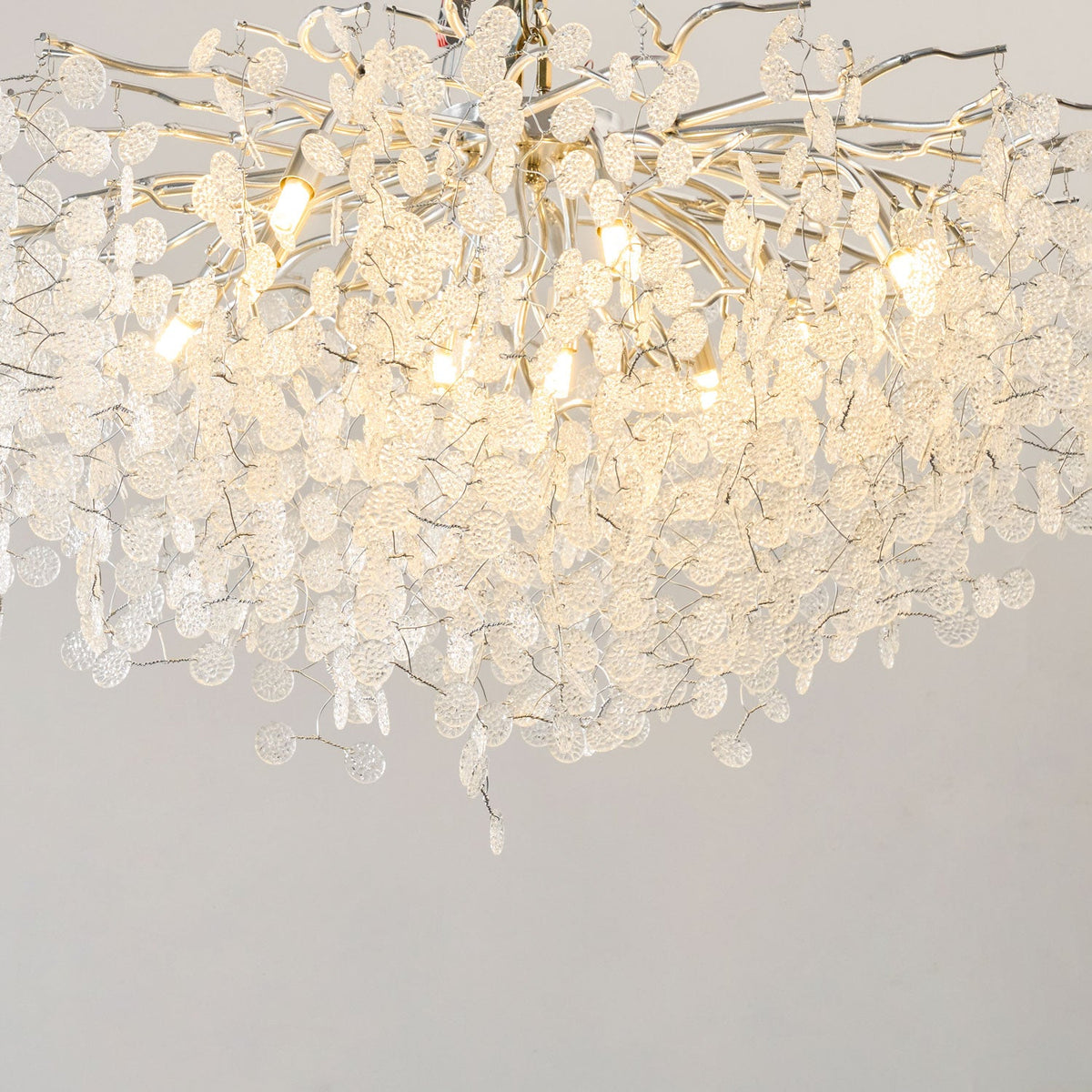 Close view of the silver branches and clear glass discs on this Clérachic ceiling light, glowing warm from within.