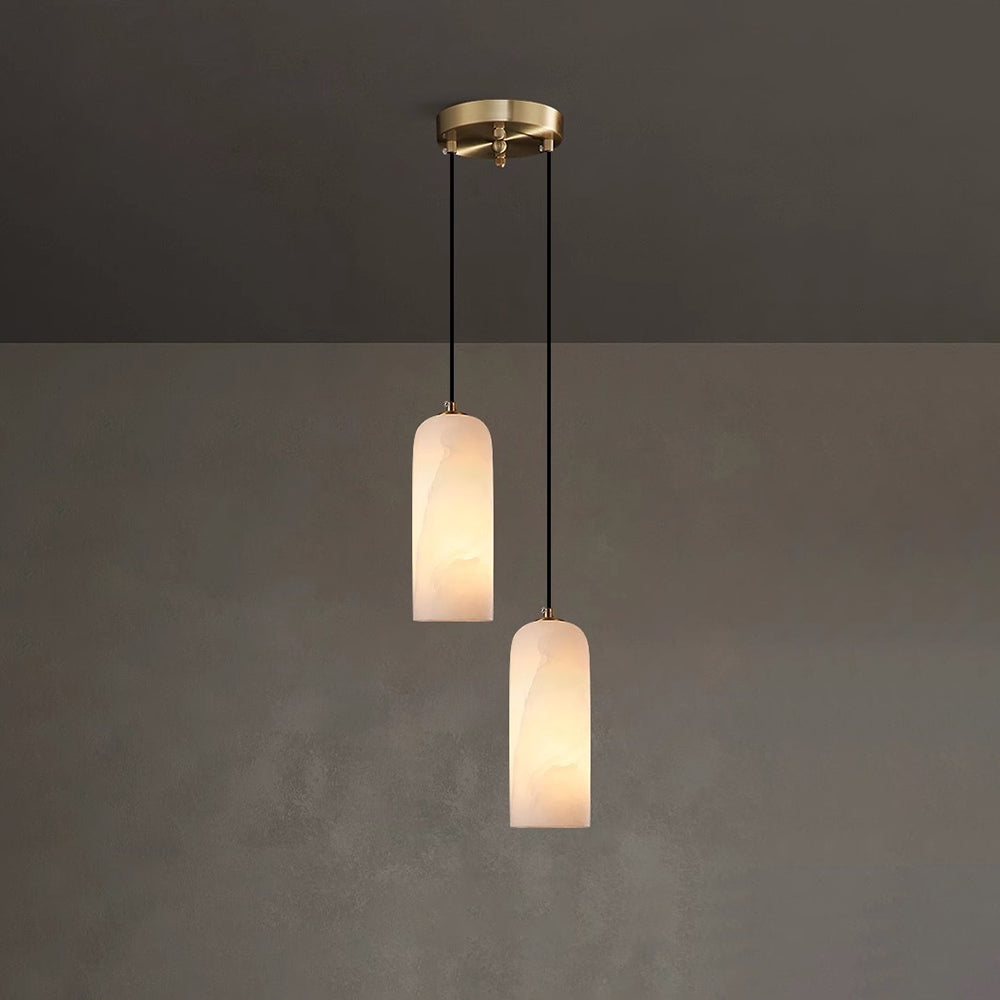 Two Hecate alabaster pendants hung at staggered drops from one round brass ceiling plate on a dark wall.