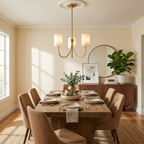 This Clérachic chandelier in brass finish is suspended over a wood dining table, a round mirror on the wall behind it.