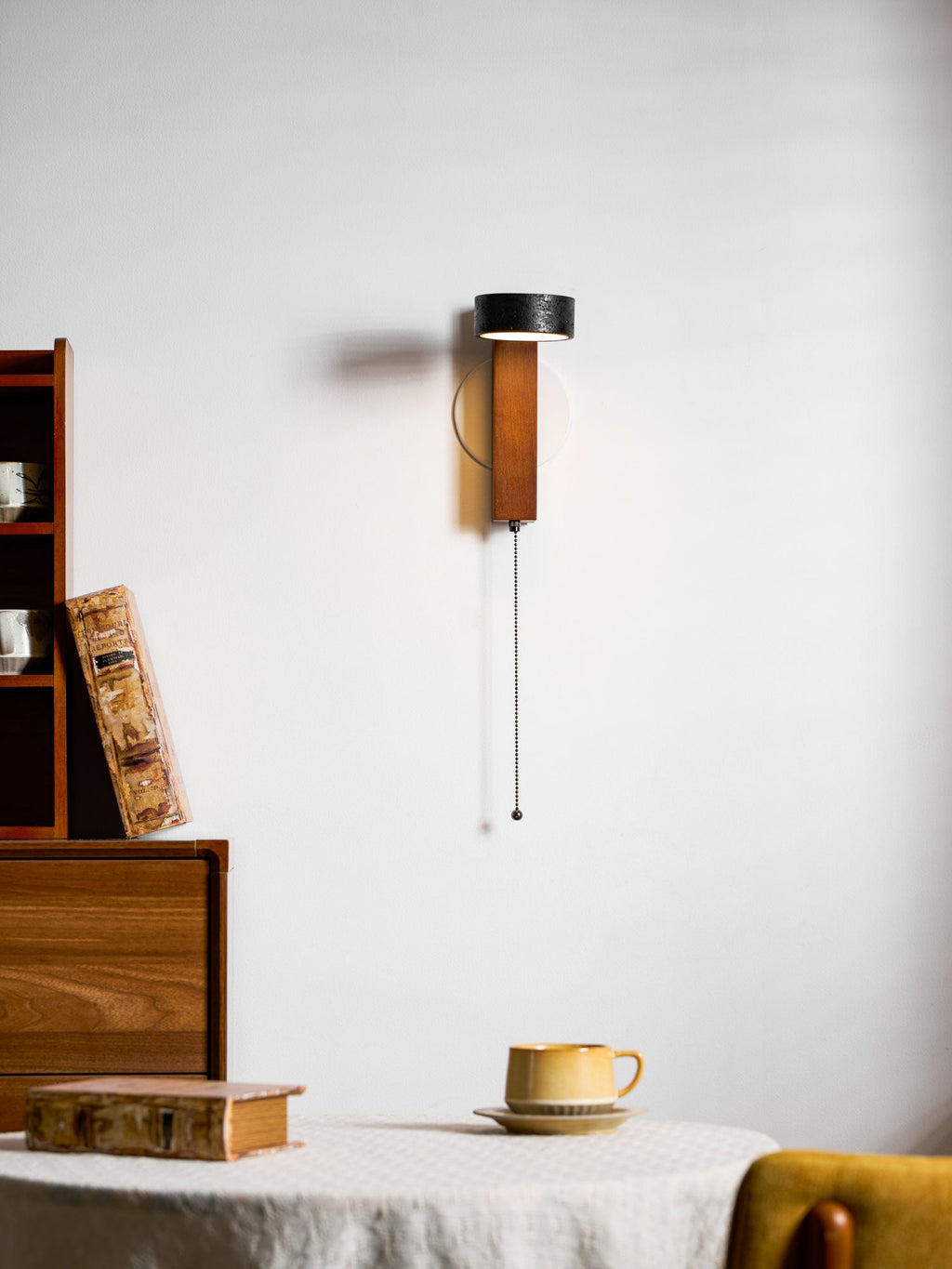 Angled toward the room, this Clérachic wall light is mounted above a table set with a book and teacup.