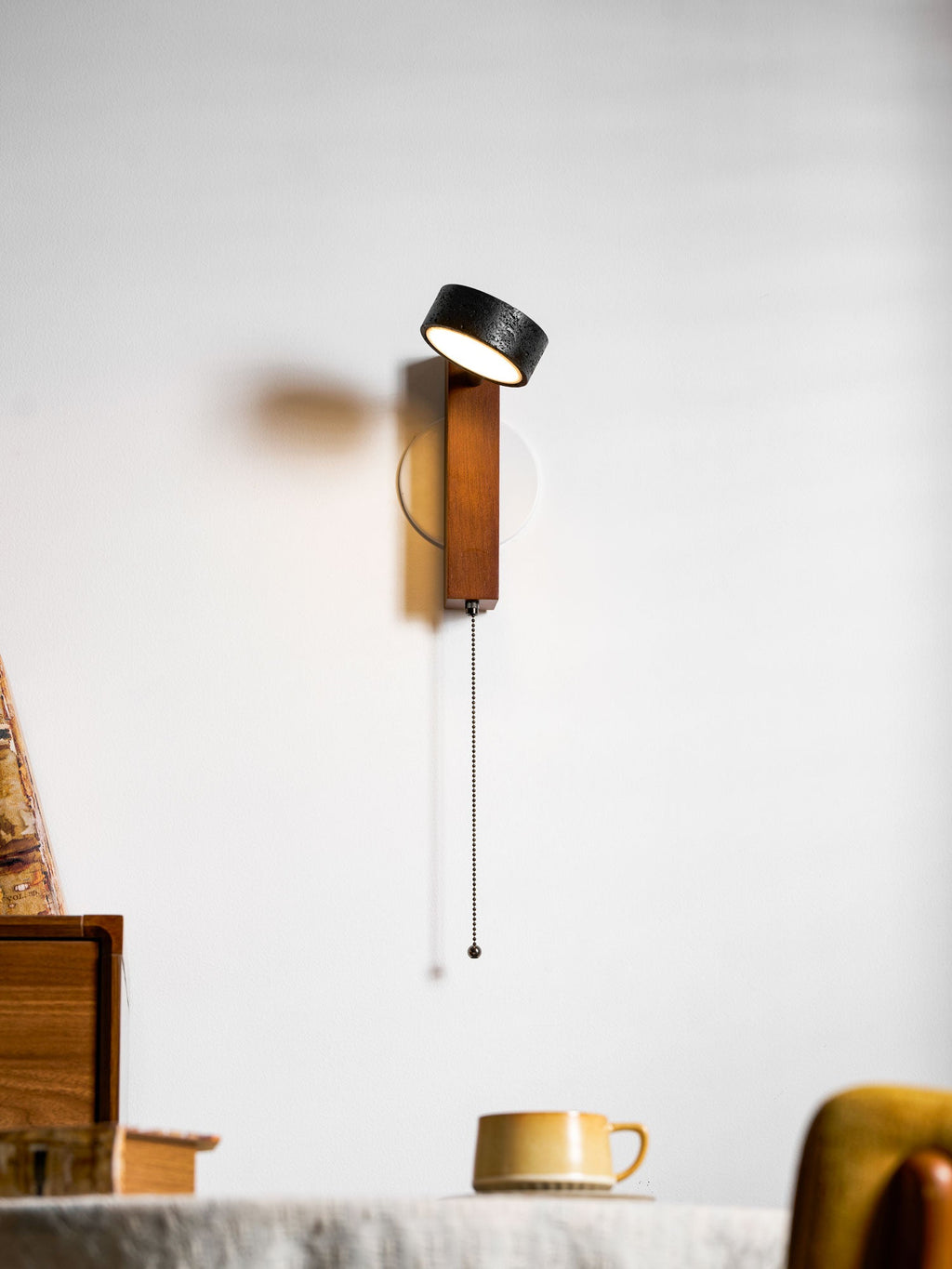 Facing straight out from the wall, this Clérachic wall light hangs beside a bookcase of cups and books.